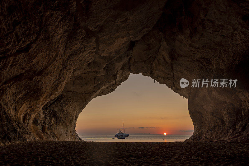 意大利撒丁岛的奥罗塞湾，Cala Luna洞穴，夕阳下，背景是帆船。